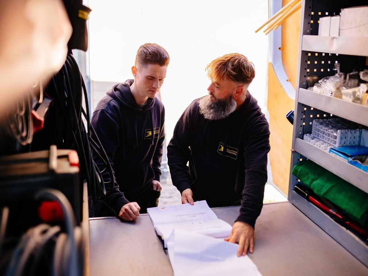 Twee collega’s van U. Veenstra bekijken samen bouwtekeningen aan de werktafel in de open werkbus, omringd door gereedschap en materialen.