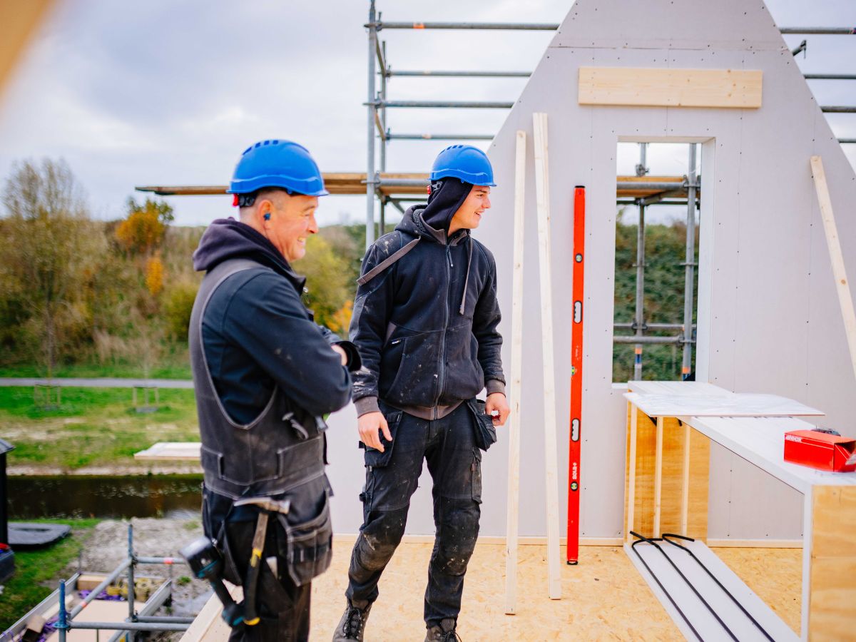 Twee timmermannen van U. Veenstra overleggen op hoogte bij de montage van een nieuwbouwwoning
