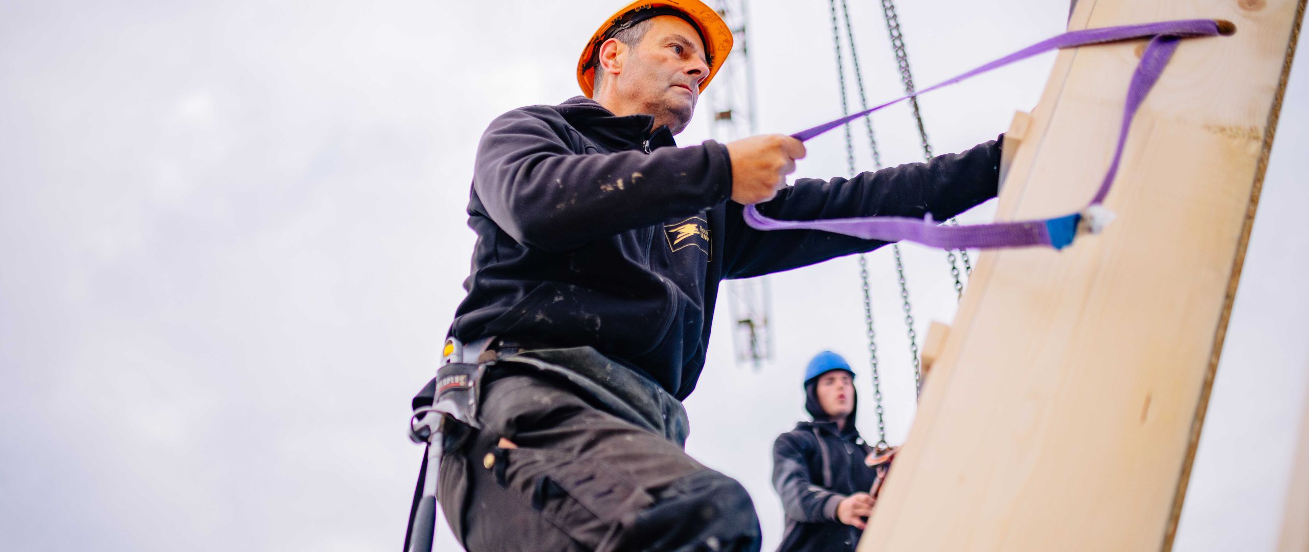 Timmerman van Bouwbedrijf U. Veenstra bevestigt een houtskeletbouwelement met hijsbanden tijdens montage op de bouwplaats