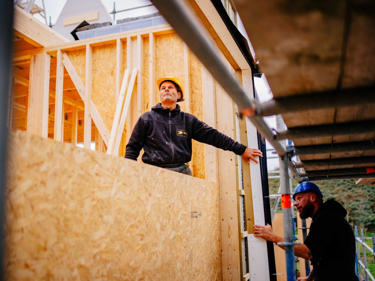 Twee timmermannen van Bouwbedrijf U. Veenstra werken samen aan de montage van houtskeletbouwwanden op de bouwplaats